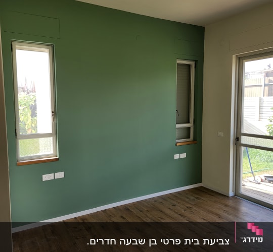 קיר צבוע בירוק עם חלונות ורצפת עץ